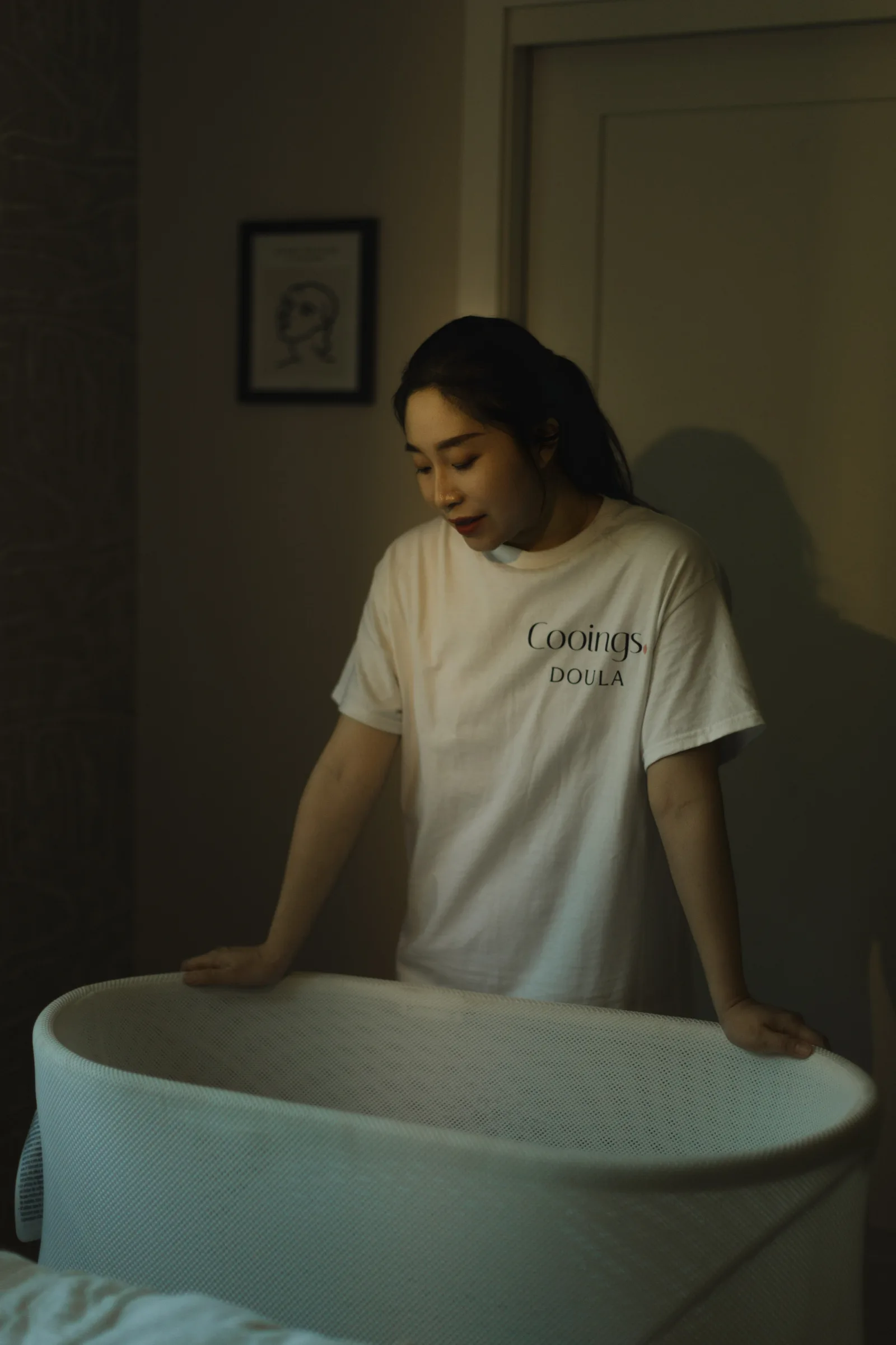 Soft window light over a parent holding a sleeping newborn, eyes lowered, calm but tired
